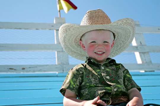 A young boy wearing a cowboy hat, sitting in the bleachers at a county fair rodeo.