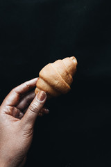 Female hand holding small croissant over black background