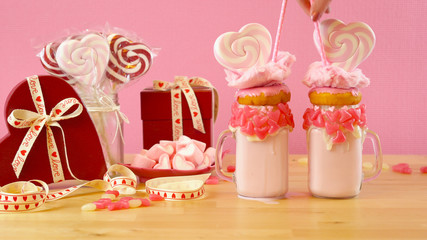 On-trend Valentine's Day table setting with pink strawberry freak shakes topped with heart shaped lollipops, donuts and cotton candy.