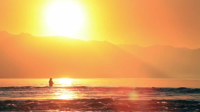 Fisherman fly fishing at sunset at the lake and mountains