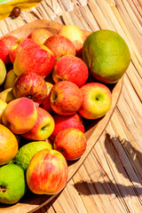 Wooden bowl and rustic straw mat with various guavas, apples, mango and bananas under the sunlight