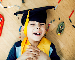 little cute preschooler boy playing toys at home happy smiling in graduation hat, lifestyle...