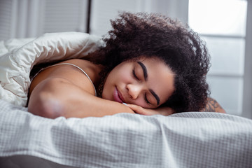 Peaceful dark-skinned woman resting on bed and having nice sleep