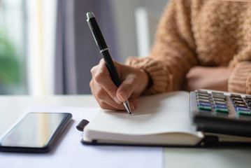 Close-up of unrecognizable woman analyzing personal finance. Lady sitting at table and writing out...