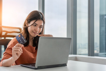 Young asian woman holding mockup credit card and use laptop for purchase product on internet in home office, Cyber Monday shopping online concept, Copy space.