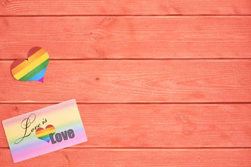 Postcard love is love and a heart with a rainbow of LGBT people in the background, lying on wooden texture background color living coral