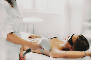 Process of laser epilation on armpit. Young woman laying on bed in a salon.