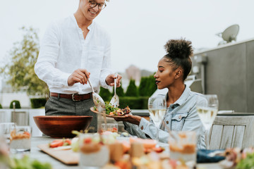 Man serving his friends salad at a rooftop party