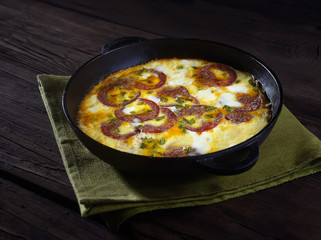 omelet with sausage and onions in a pan on a wooden background.  rustic style.