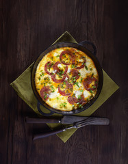 omelet with sausage and onions in a pan on a wooden background. top view. rustic style.