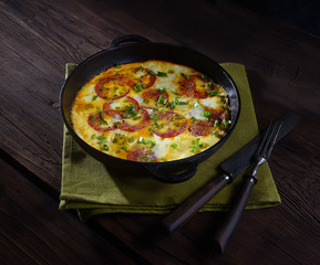 omelet with sausage and onions in a pan on a wooden background.  rustic style.