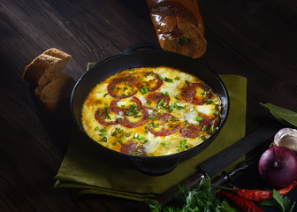omelet with sausage and onions in a pan on a wooden background.  rustic style.