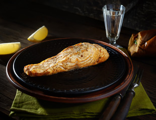 Baked salmon steak on a black plate on wooden background. rustic style.