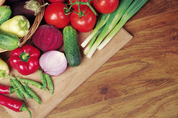 Vegetables on the kitchen board on a wooden table. Cabbage, cauliflower, cucumbers, tomatoes, peppers, corn, peas, onions, 