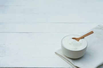 Plain yoghurt in white bowl and wood spoon on white wooden table background
