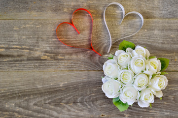 A bouquet of white roses and two hearts of white and red on a wooden background.