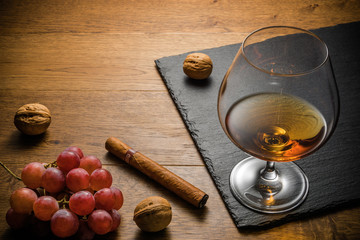 Glass of cognac and cigar with snack on the wood table with stone cutting board. Top view with copy...