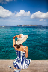 Happy woman in hat relaxing on sea pier in Sardinia island, Italy