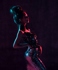 Beautiful fashion sexy brunette woman posing in blue and pink neon light in fashion gold sparkle...