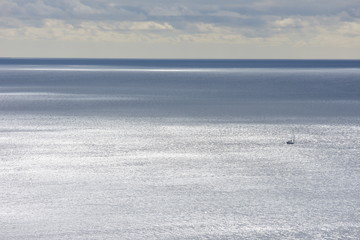 View of sea surface changing its color from silver to dark gray with lone tiny sailing ship being just small spot in vast ocean.