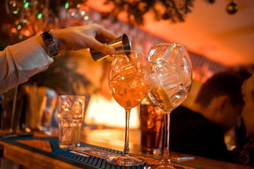 Bartender garnishing on the counter three Aperol Spritz, a classic refreshing Italian aperitif made mixing Aperol, Prosecco and sparkling soda to enjoy with friends and family at the bar before meals.