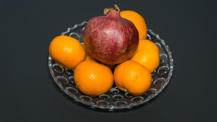 several pomegranates and tangerines on a plate on a black background