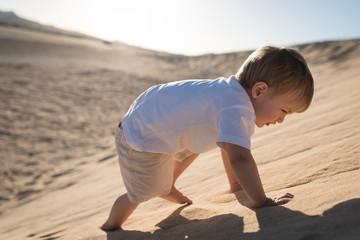 Little boy climbing on a sand dune.