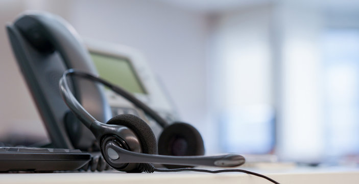 close up soft focus on headset with telephone devices at office desk for customer service support concept 