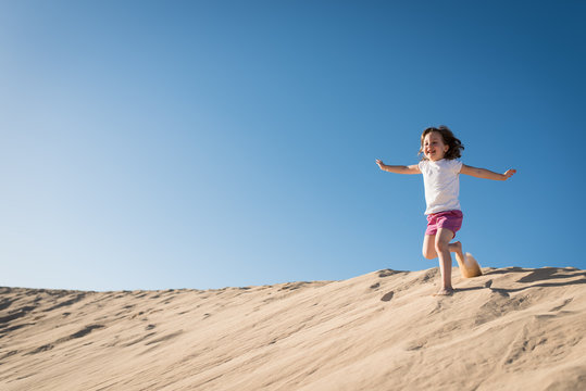 Happy girl running down sand dune
