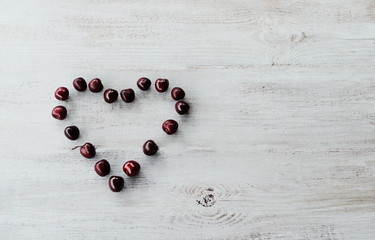 red sweet cherry laid out on a light wooden background in the form of heart 