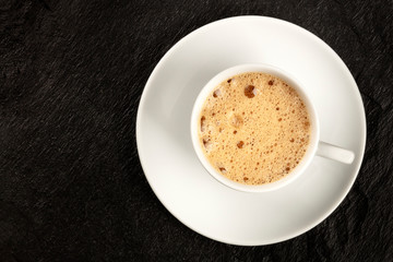 A photo of a cup of coffee with foam, shot from above on a dark black background with copy space