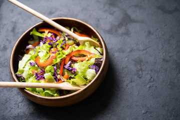 Fresh vegetables salad with purple cabbage, white cabbage, lettuce, carrot in dark clay bowl on black background.