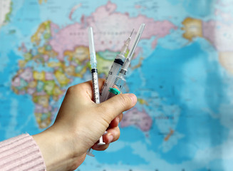 The hand of a woman with three disposable syringe against the backdrop of a world map.
