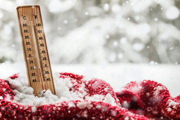 thermometer with sub zero temperature sticks out in a snowdrift wrapped red scarf