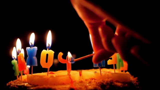 slow motion closeup hand lights candles on birthday cake decorated with pineapple in dark background