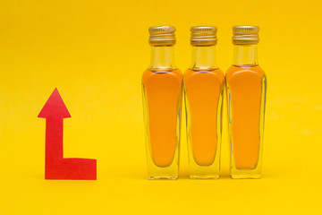 Small bottles of alcohol on a yellow background and a red arrow concept of raising the price of alcohol, close-up, markup