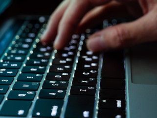 Close up of fingers touch laptop keyboard with backlit, side view. Focus on keyboard buttons