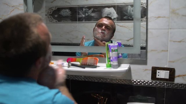 A man soaping face with soap in front of a bathroom mirror