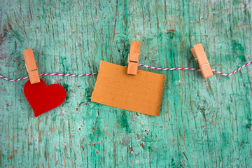 old blank paper and paper red heart hung on clothespins on a rope on a mint green wall background