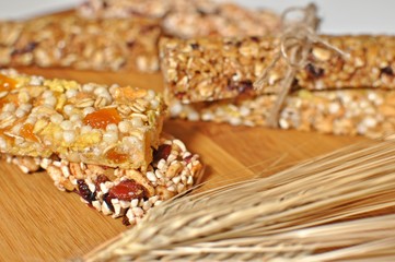 Side view close up of sweet slices of healthy cereal bars with dried wheat and fruits on brown wooden table background