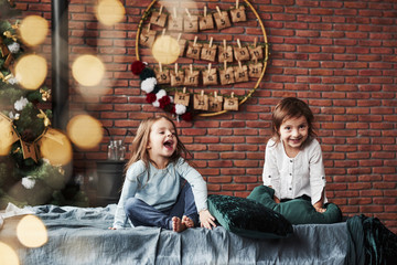 Loud laughing. Little girls having fun on the bed with holiday interior at the background