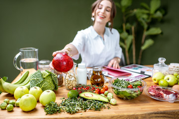 Woman dietitian in medical uniform working on a diet plan sitting with different healthy food ingredients in the green office