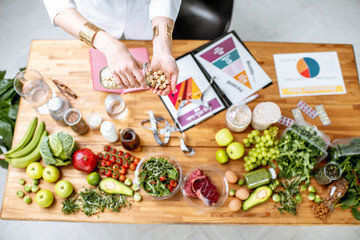 Dietitian holding nuts above the table full of various healthy products and drawings on the topic of healthy eating