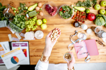 Dietitian holding nuts above the table full of various healthy products and drawings on the topic...