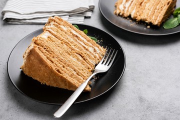 Layered honey cake on black plate. Russian Medovik cake with many biscuit layers and custard cream