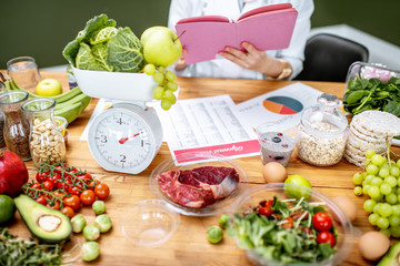 Woman dietitian working on a diet plan sitting with various healthy food ingredients, cropped image...