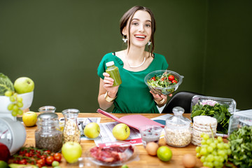 Portrait of a beautiful woman as a dietitian sitting with smoothie, salad and various healthy food...