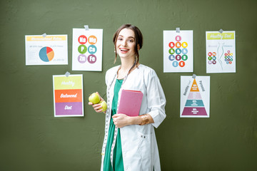Portrait of a woman dietitian in medical gown standing on the green wall background with drawings...