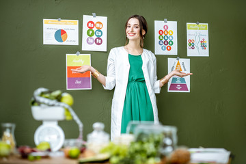 Portrait of a woman dietitian in medical gown standing on the green wall background with drawings...