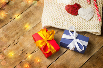 Two hearts, knitted scarf, gift boxes, luminous garland on a wooden background. The concept of lovers, Valentine's Day, a gift for a loved one. Flat lay, top view.